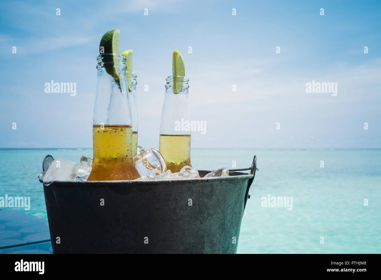 Lime slices in beer bottles on ice on tranquil ocean beach, Maldives