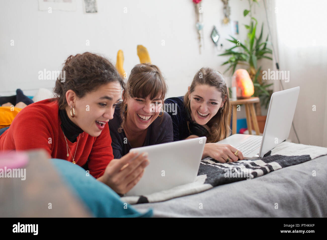Young women friends hanging out, using digital tablet and laptop on bed Stock Photo