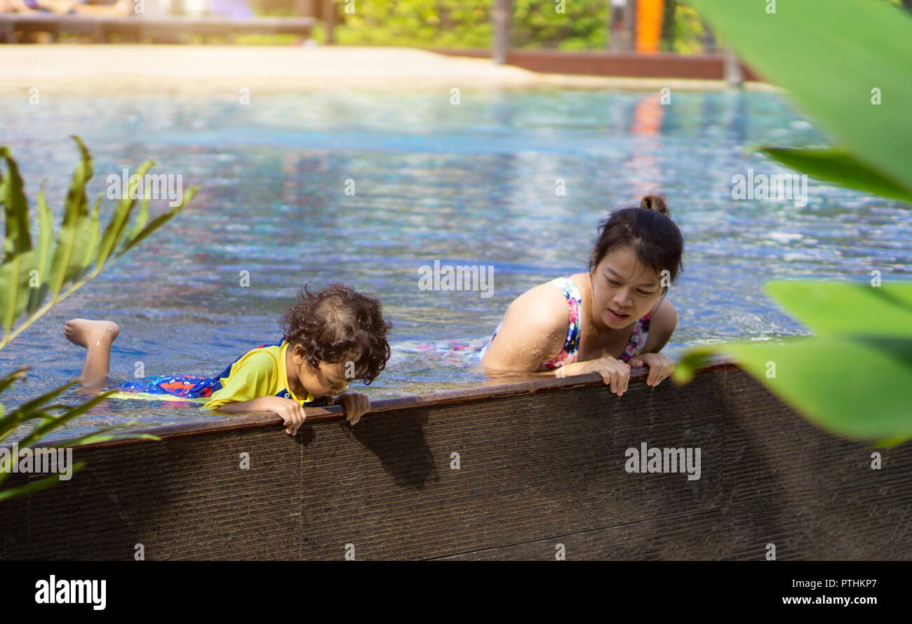 Asian child boy learn swimming in a swimming pool with mom. - Sunset filter effect. Stock Photo
