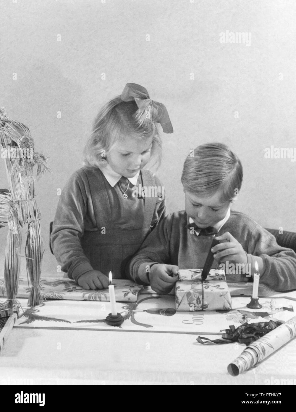 Christmas in the 1940s. Two well dressed children are wrapping christmas presents. The boy is melting wax and dripping it onto the gift package. Usually a stamp is put in the hot wax with the words Merry Christmas. Sweden 1940s Stock Photo