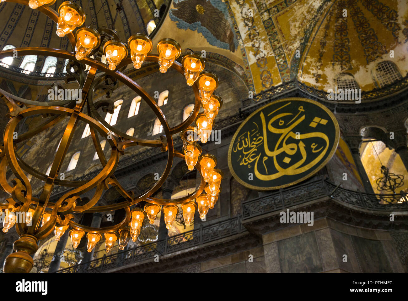 View of on of the chandaliers that light up the main nave interior of the Hagia Sophia museum with dome and calligraphic roundel in background, Istanb Stock Photo