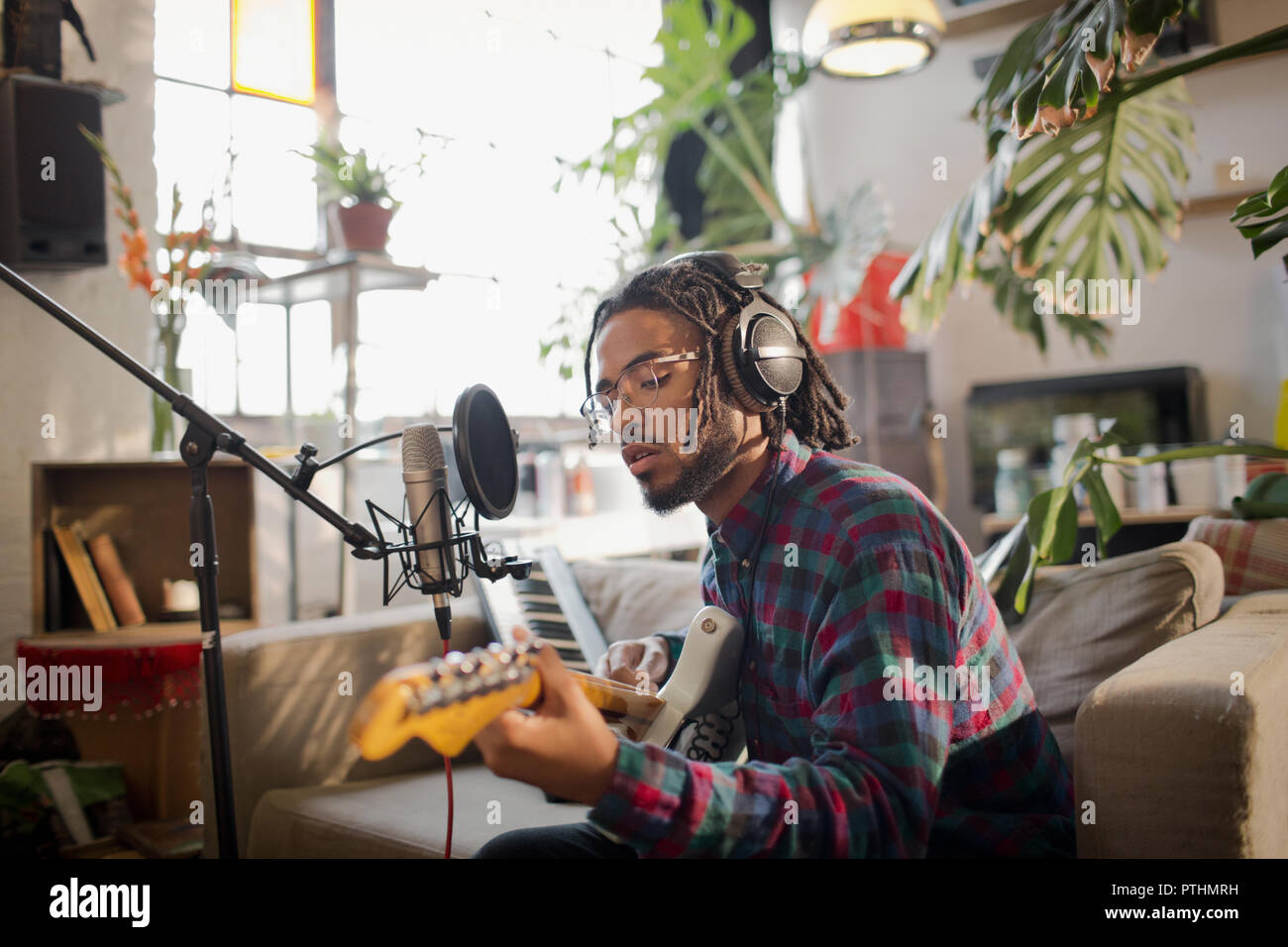 Young male musician recording music, playing guitar at microphone in
