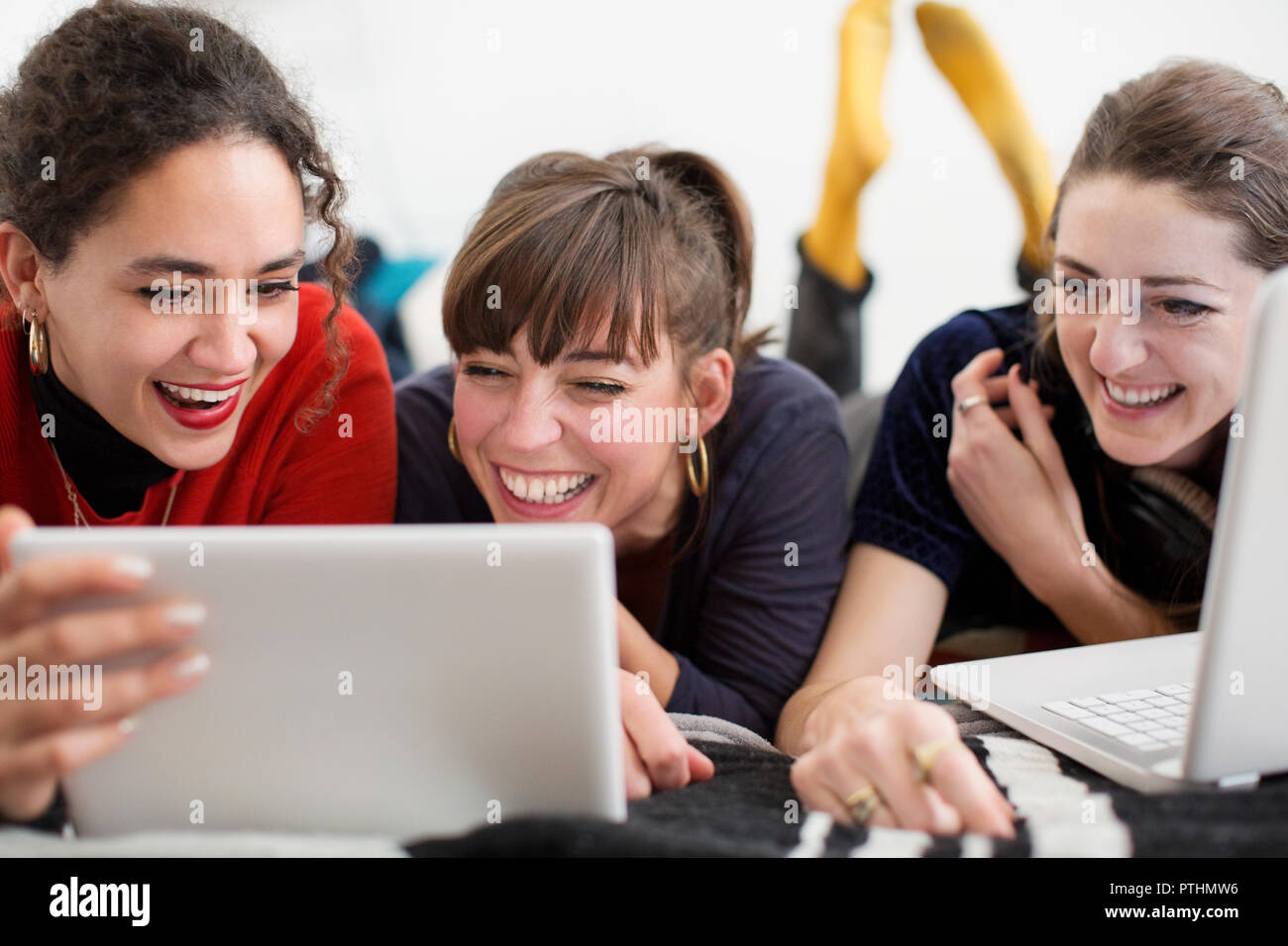 Laughing young women friends hanging out, enjoying digital tablet and laptop on bed Stock Photo