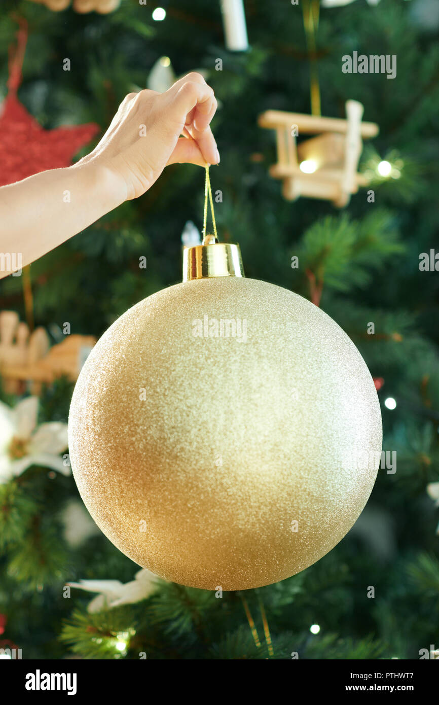 Closeup on young woman in red dress near Christmas tree hanging big gold  Christmas ball Stock Photo - Alamy