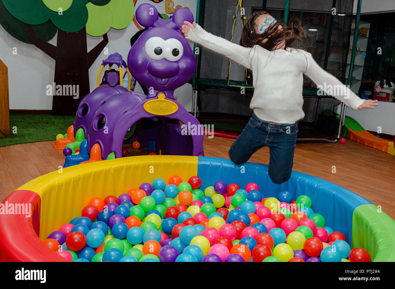 Little girl throwing herself in a pool full of colorful balls at a