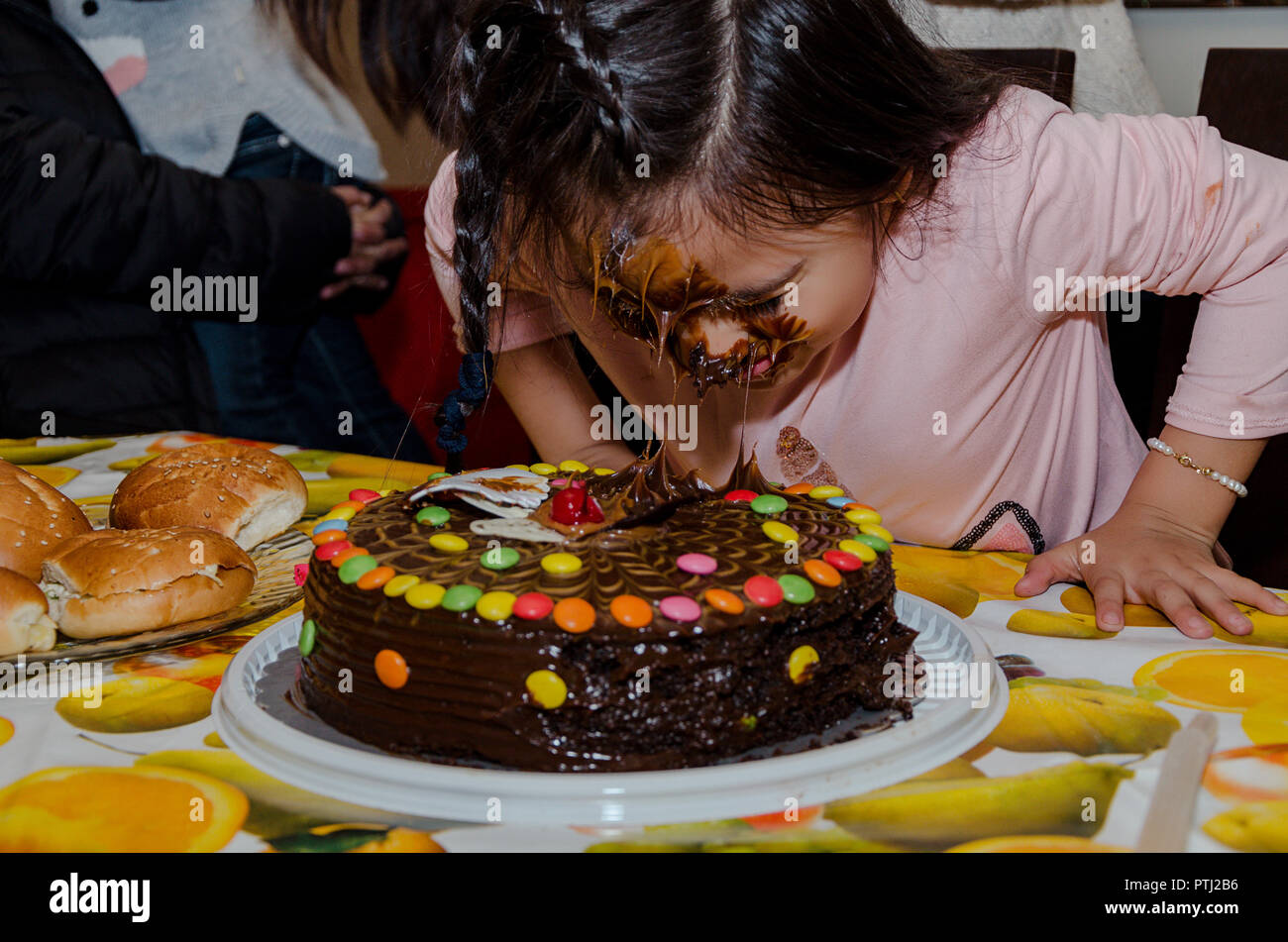 6 year old girl celebrating her birthday by putting her face inside the chocolate cake Stock Photo