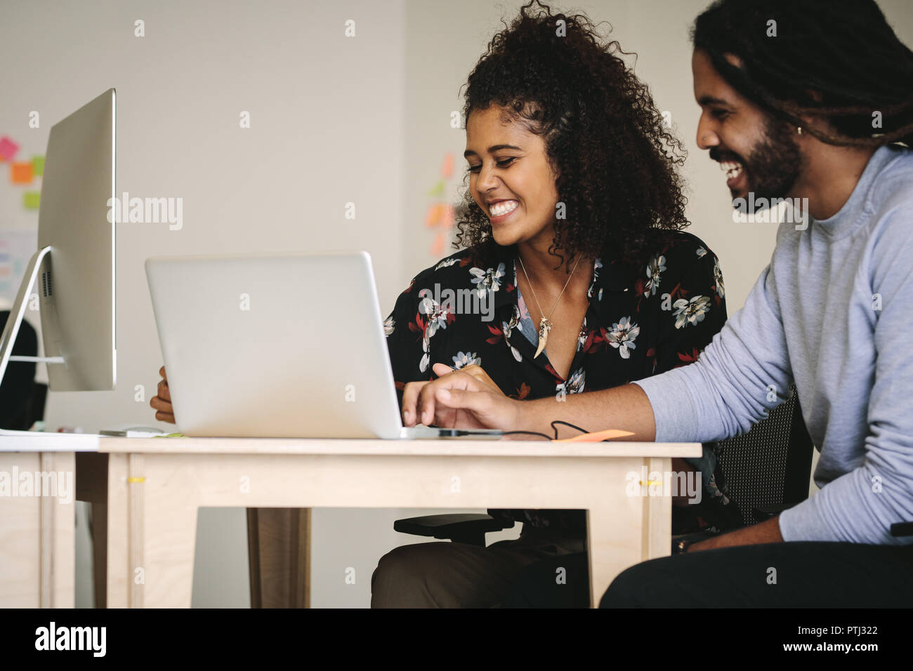 Business partners sharing ideas sitting at the desk with laptop computer. Happy business colleagues in office working on a project together. Stock Photo