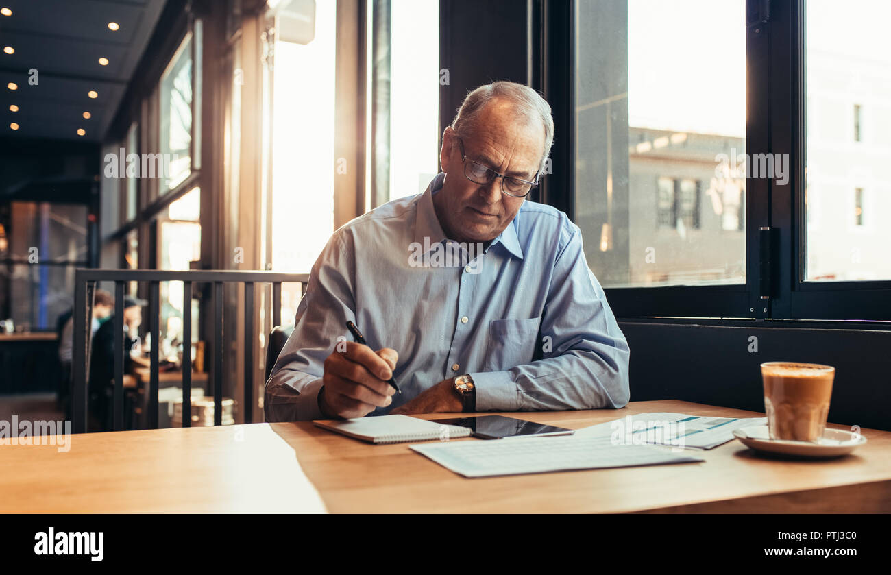 Mature businessman making notes while sitting at cafe. Senior man at modern coffee shop working. Stock Photo