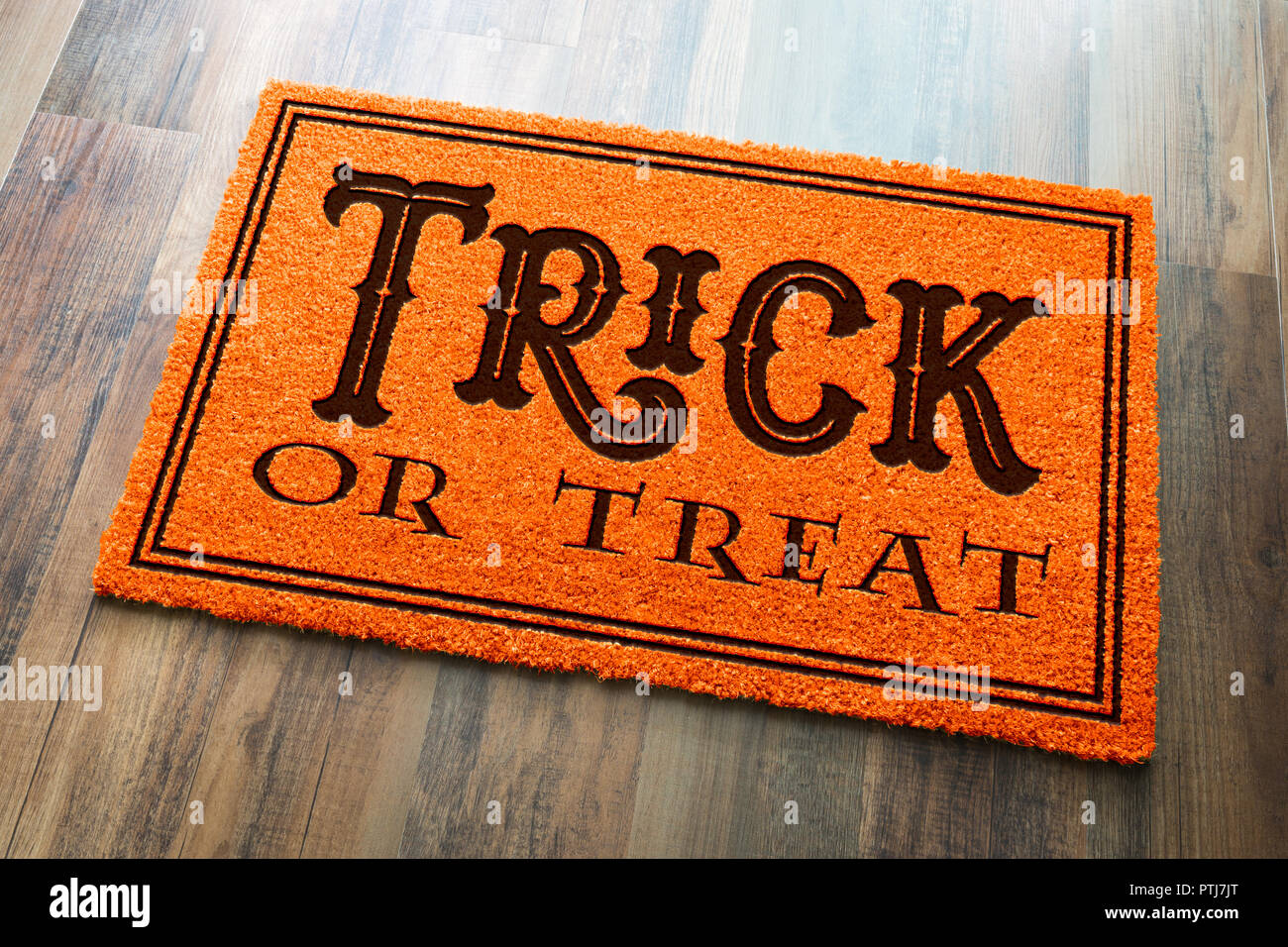 Trick Or Treat Halloween Orange Welcome Mat On Wood Floor Background. Stock Photo