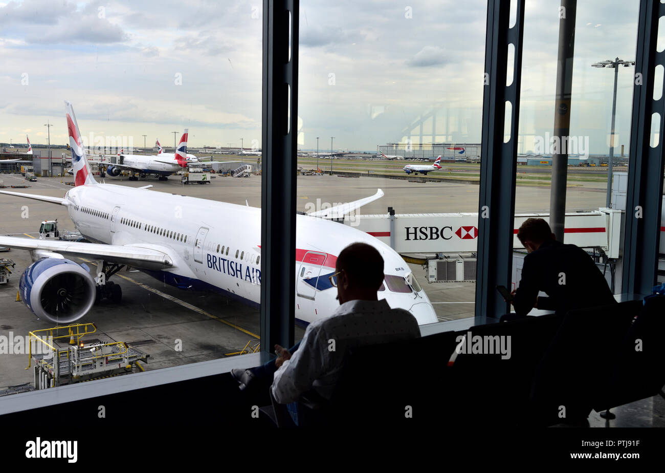 Inside airport departure two people in silhouette looking out window at plane, Heathrow, Terminal 5, British Airways Stock Photo