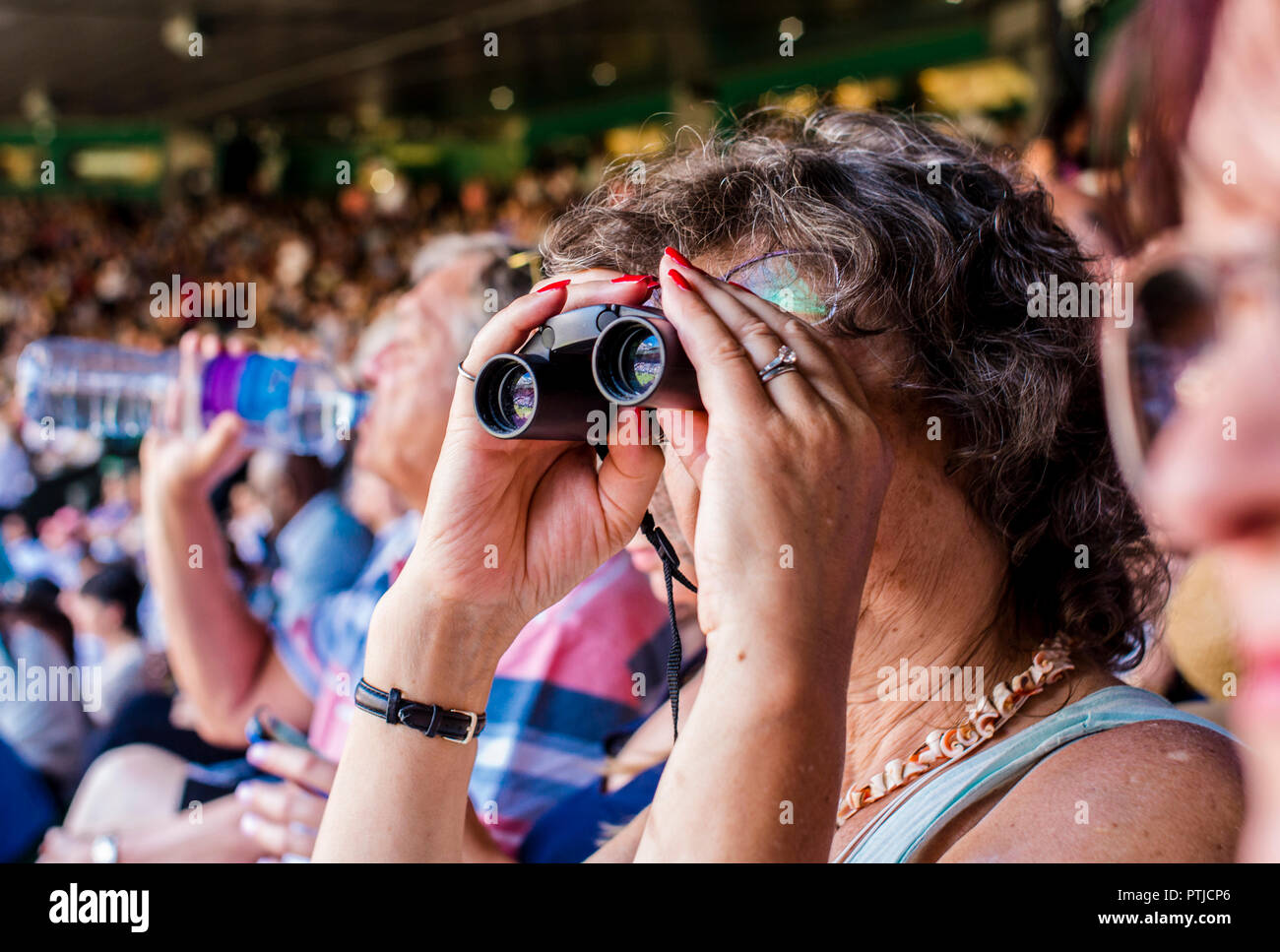 A tennis fan uses her binoculars to watch the match in Centre Court on the first day of the Wimbledon Championships. Stock Photo