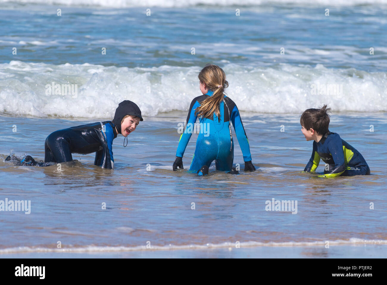 Three children wearing wetsuits playing in the sea at Fistral Beach in