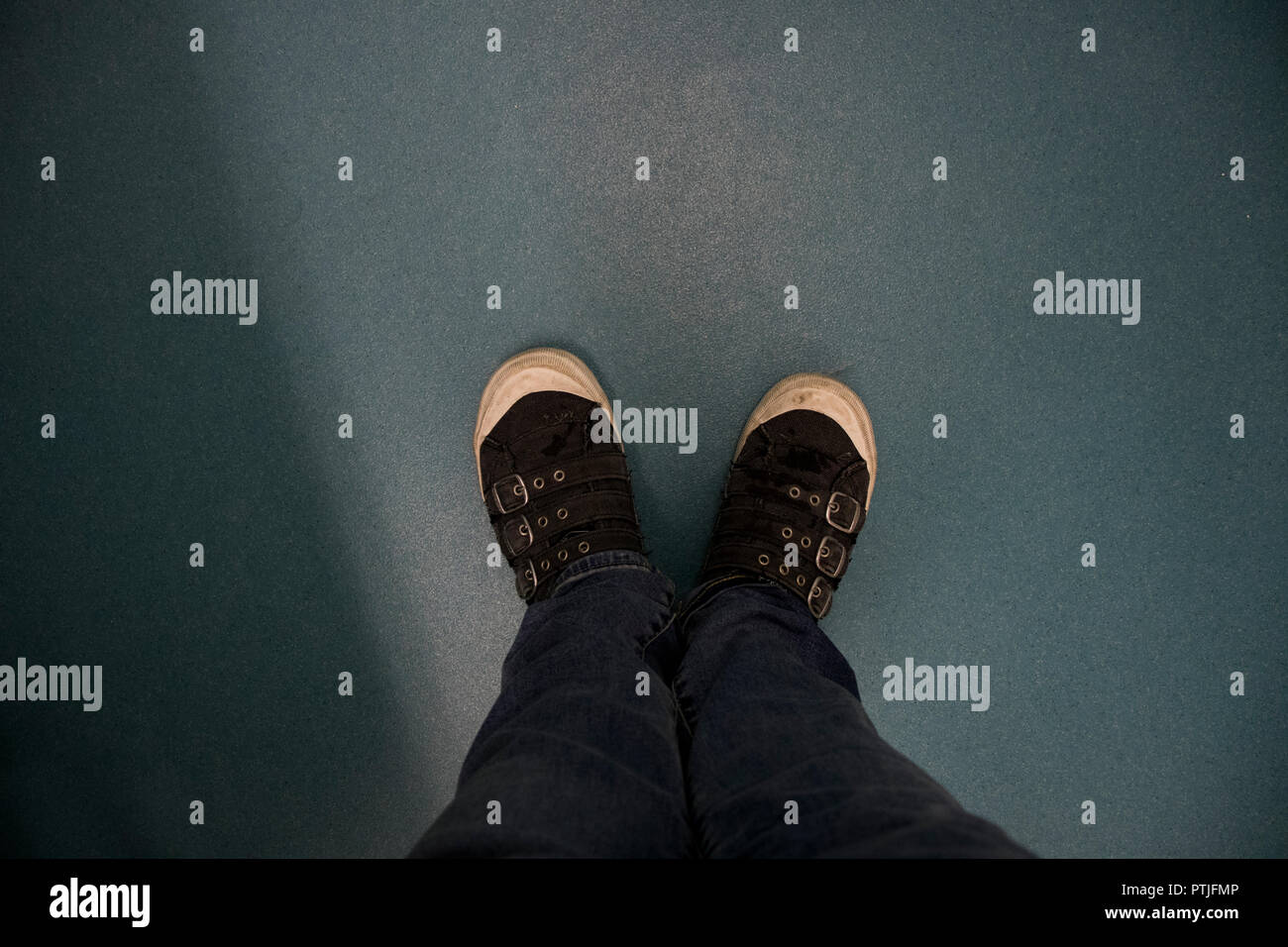 Looking down at a pair of legs and shoes standing on a hard surface