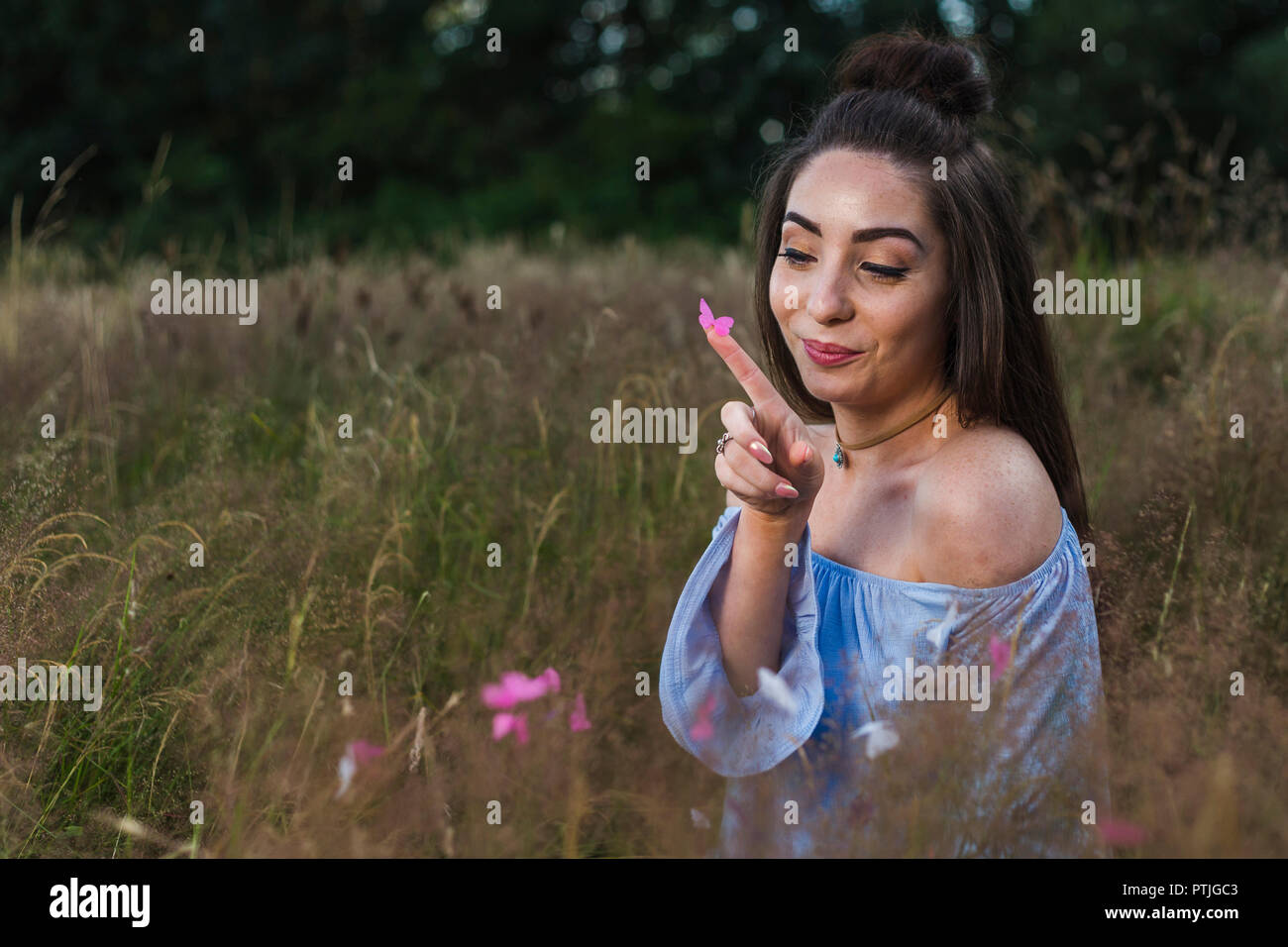 A young woman looks at a pink butterfly on the end of her finger. Stock Photo