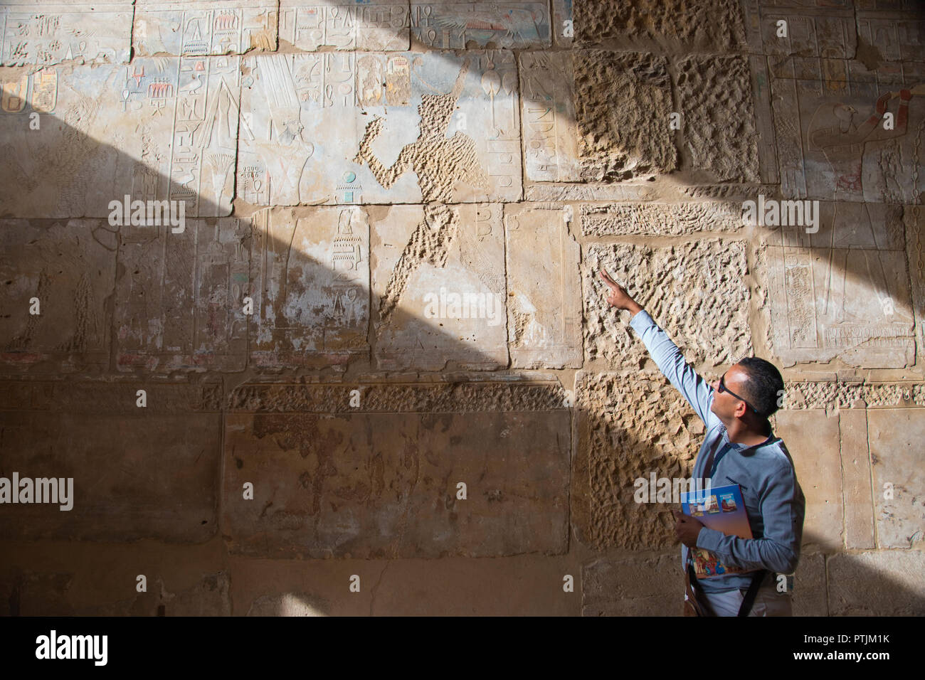 A tour guide explains how early Christians carved off brightly painted, bas relief stone images of the Egyptian gods and pharaohs inside Karnak Temple Stock Photo