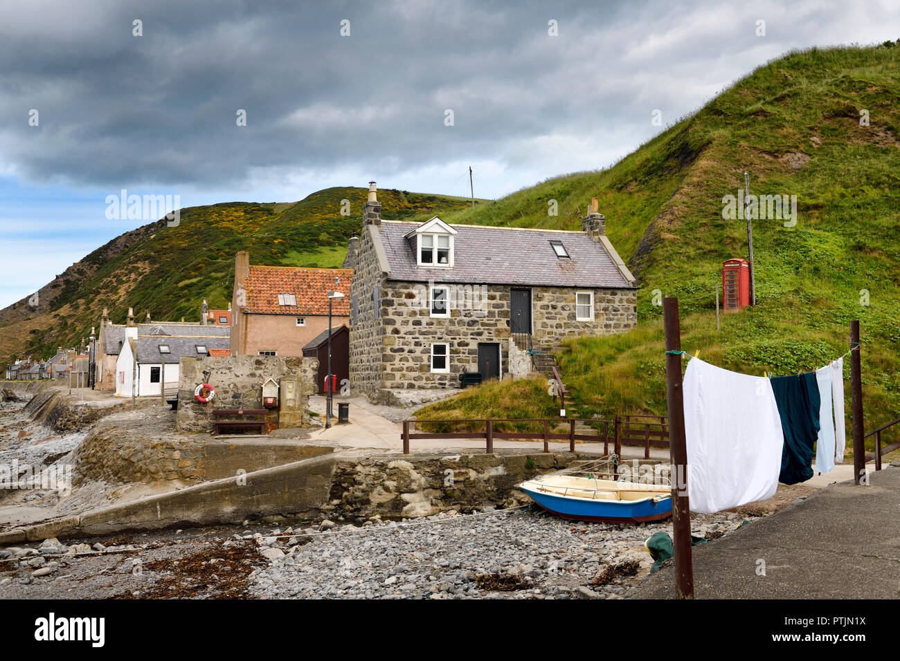 Single row of houses of Crovie coastal fishing village on Gamrie Bay North Sea Aberdeenshire Scotland UK with red telephone box and wash on line Stock Photo