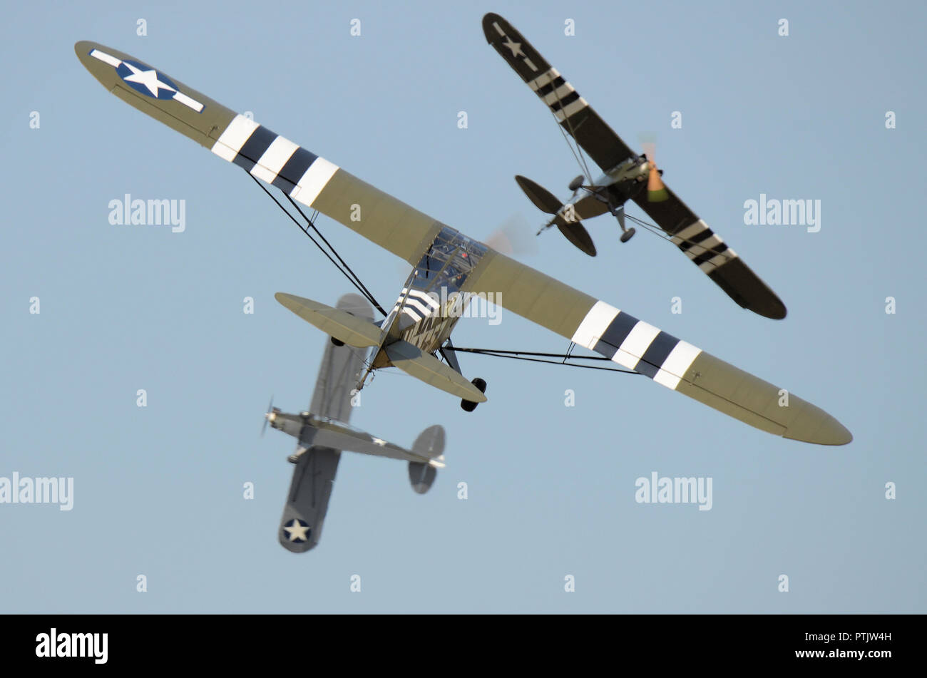 Trio of L4 Cub planes flying at an airshow. Piper L-4 Grasshopper military version of Piper J-3 Cub. D-Day invasion stripes. Spotter planes breaking Stock Photo