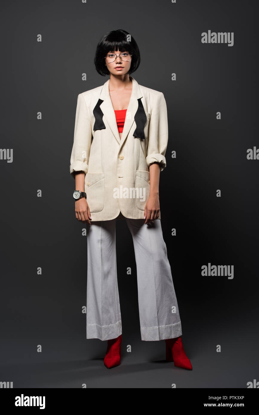 fashionable young woman in stylish jacket and bell-bottoms on grey Stock Photo