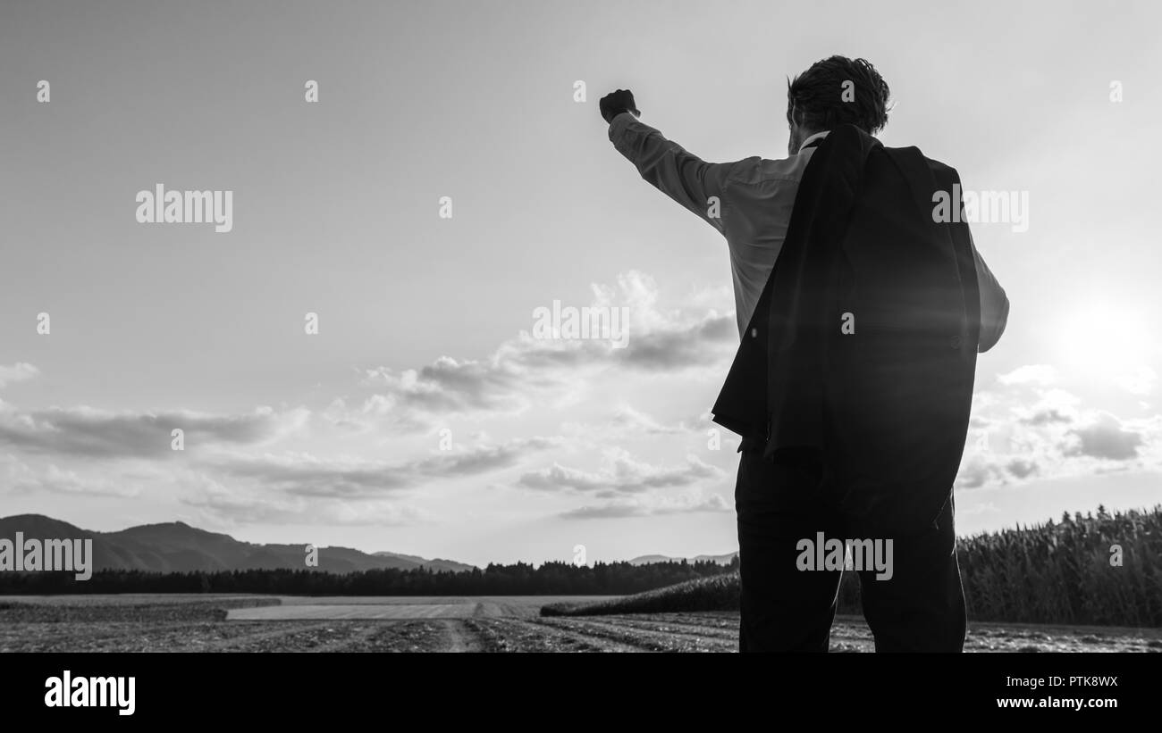 Businessman celebrating his success standing in evening nature with his jacket over his shoulder and one arm raised up high in celebration. Stock Photo