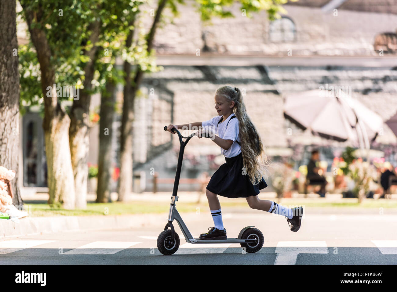 side view of adorable happy schoolchild with backpack riding scooter on street Stock Photo