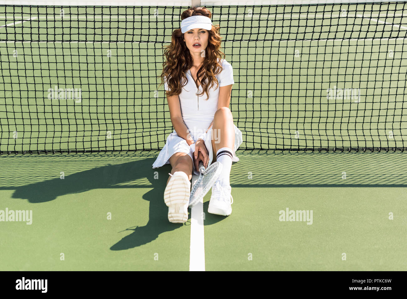 attractive woman in tennis uniform with racket sitting near net on court  Stock Photo - Alamy