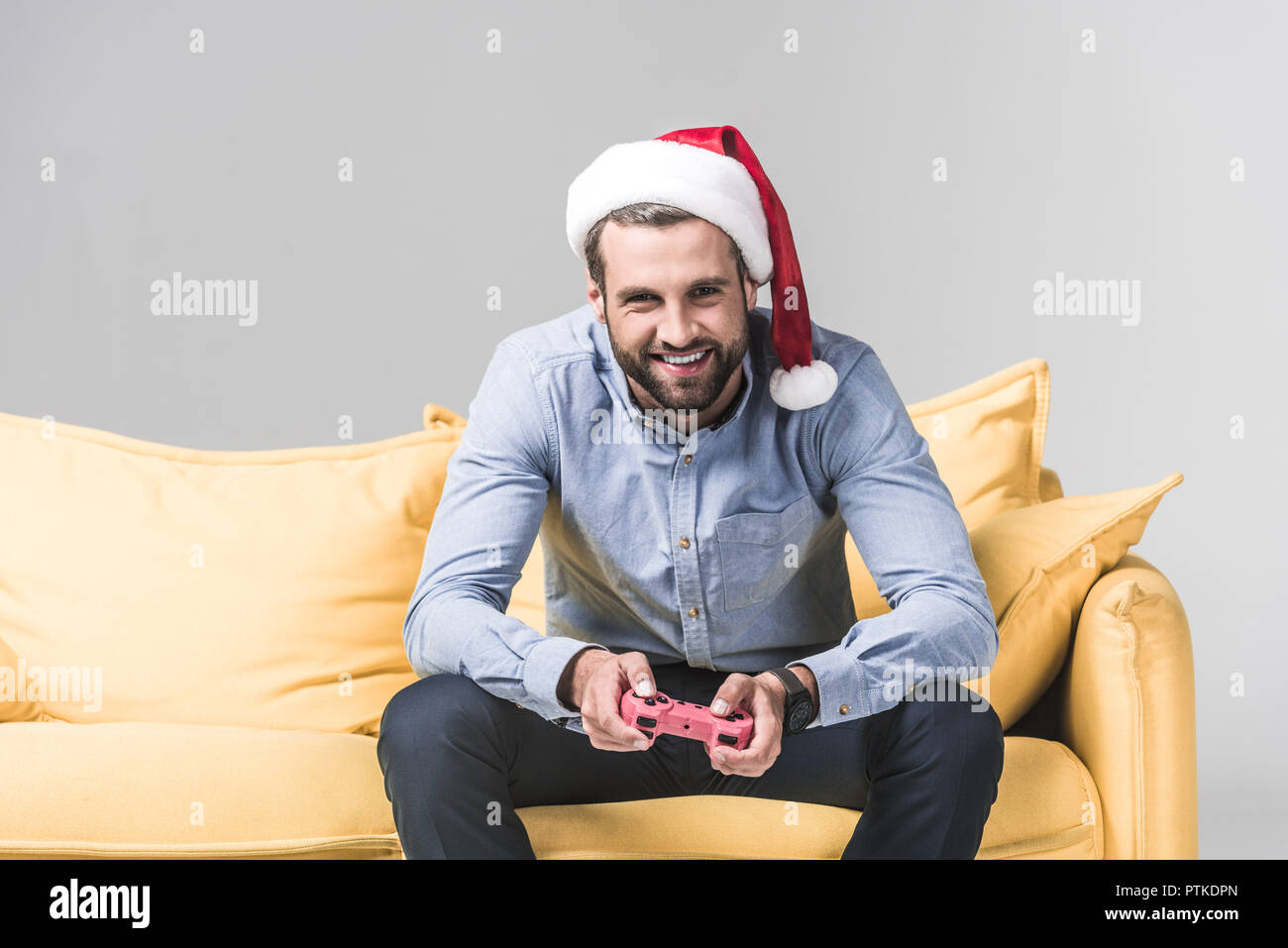 smiling bearded man in santa hat playing video game with joystick on grey Stock Photo