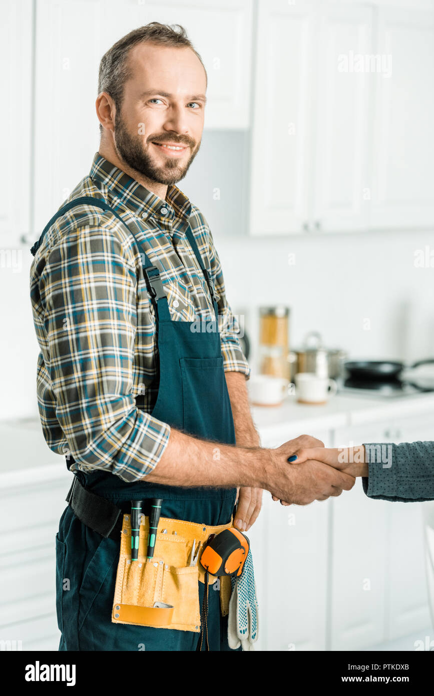 smiling handsome plumber and customer shaking hands in kitchen Stock Photo