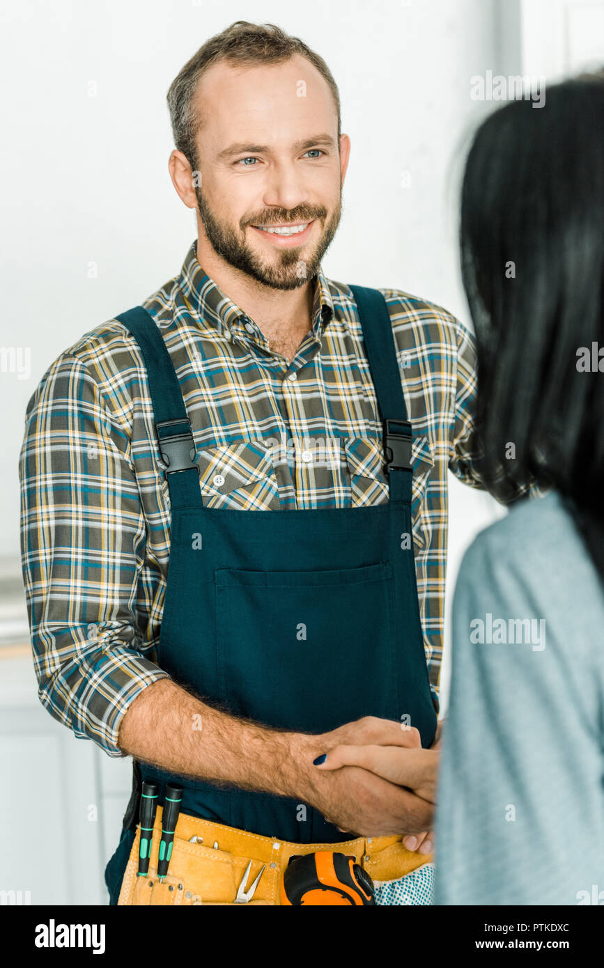 smiling handsome plumber and client shaking hands in kitchen Stock Photo