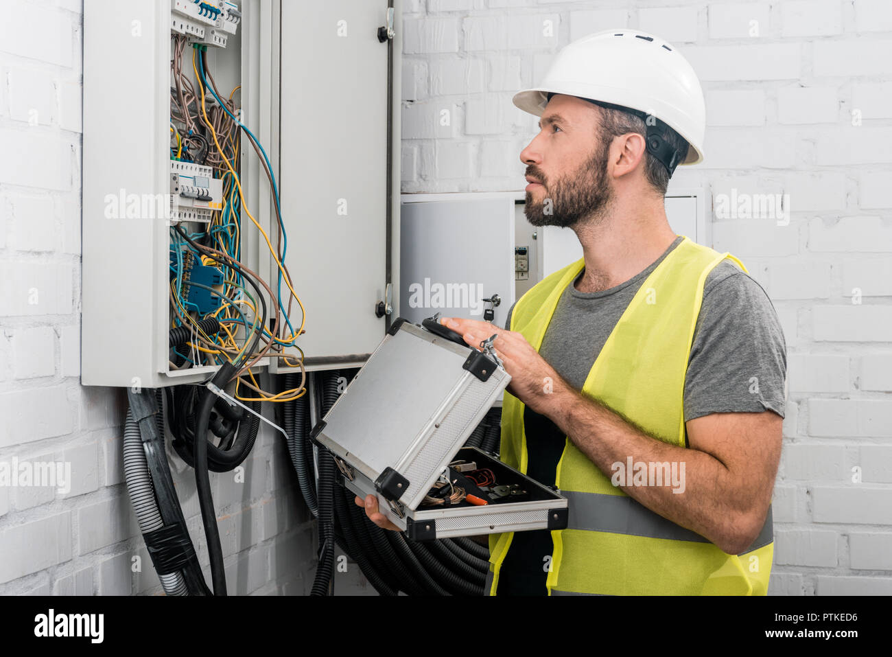 side view of handsome electrician holding toolbox and looking at