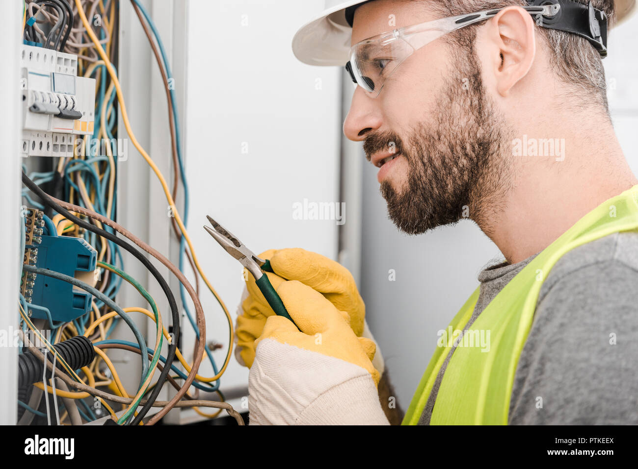 side view of handsome electrician holding pliers and looking at