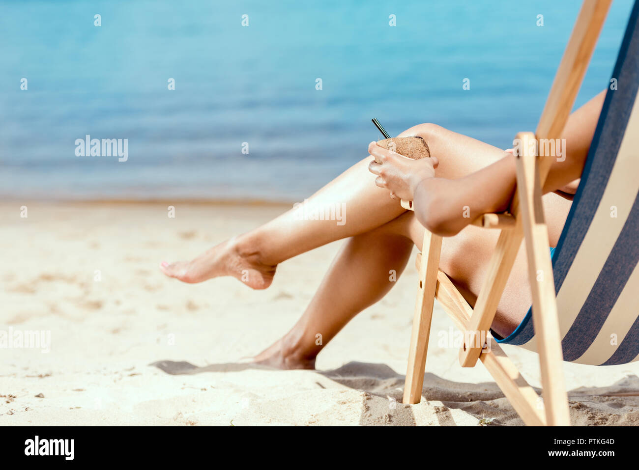 Cropped Image Of Woman Holding Cocktail In Coconut Shell And Laying On Deck Chair On Sandy Beach Stock Photo Alamy
