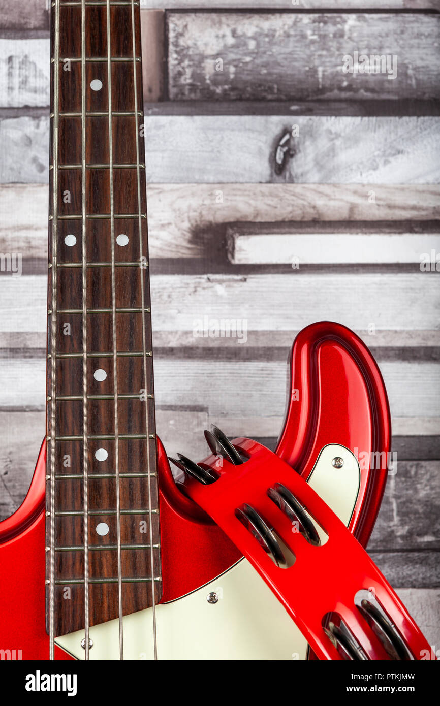 Red electric base guitar leaning against a wooden clad wall with a red tambourine hanging from it Stock Photo