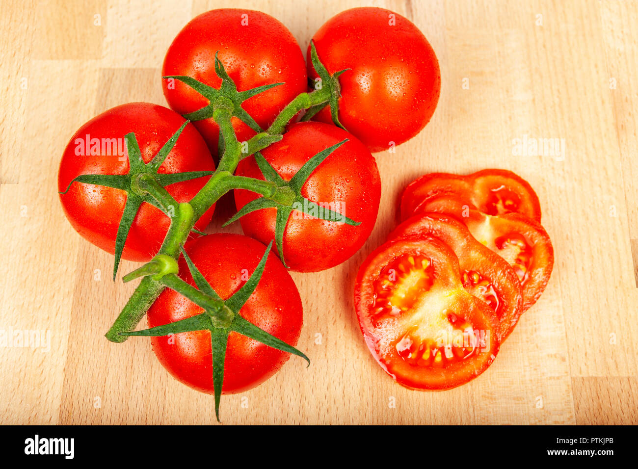 Fresh ripe tomatos on a vine on a wood block chopping board aside some chopped jucy slices Stock Photo