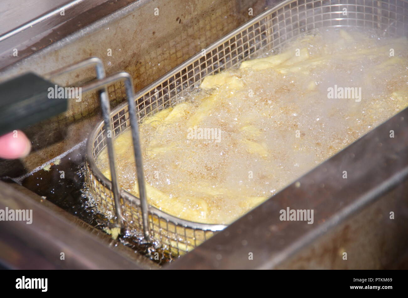Frittieren von French Fries und Pommes Frites in einer sprudelnden und schmutzigen Fritteuse mit Metallkorb und viel Frittierfett bzw. Öl Stock Photo