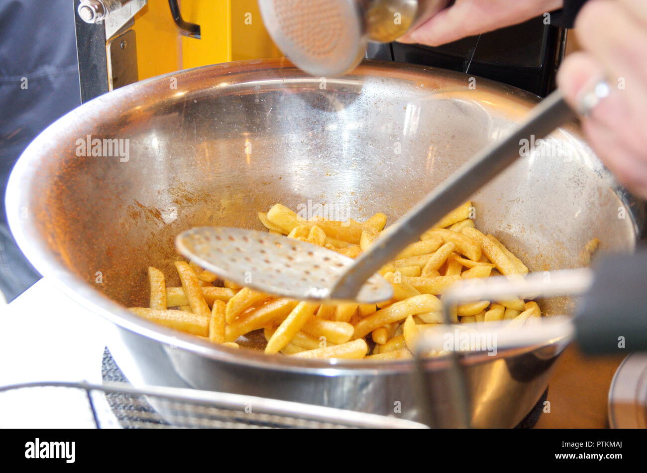 Im Foodtruck von einem Imbiss würzt jemand Pommes Frites / French Fries in einer Edelstahl Metallschüssel mit viel Salz und Paprika Gewürz Stock Photo