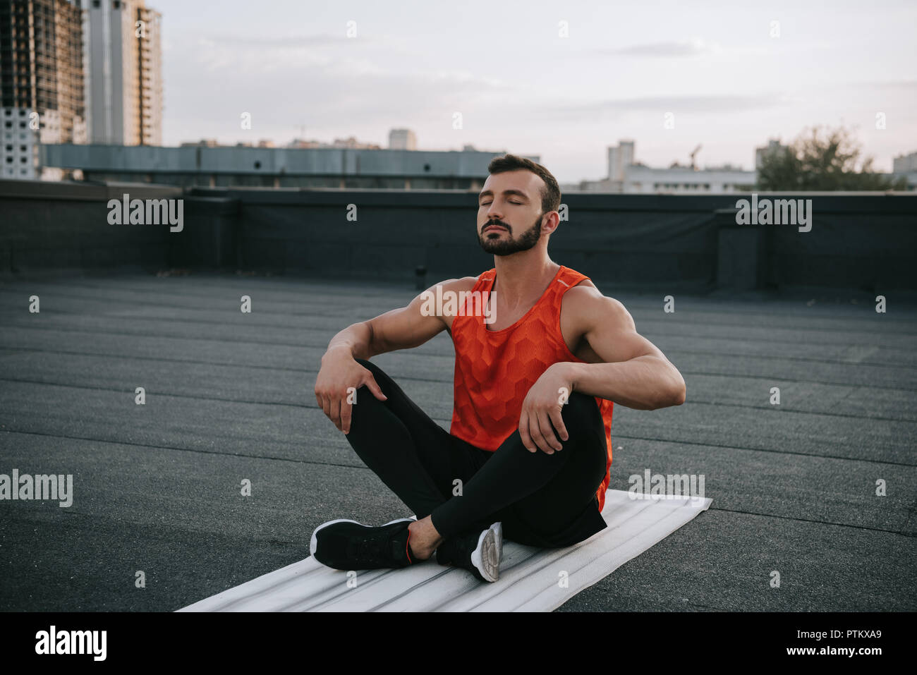 handsome sportsman stretching legs on yoga mat on roof Stock Photo