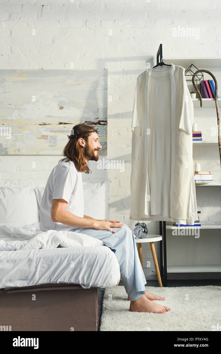 side view of happy Jesus sitting on bed during morning time in bedroom
