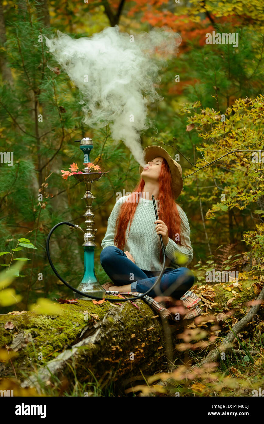 Young redhead woman in hat smoking Hookah in forest Stock Photo Alamy