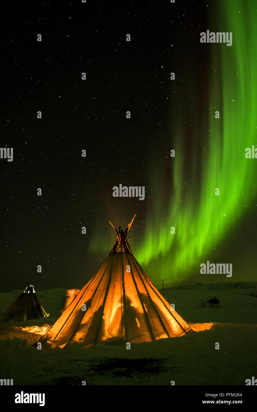 Friends keep warm in a traditional Sami tent under the Northern lights near Tromso in Northern Norway. Stock Photo