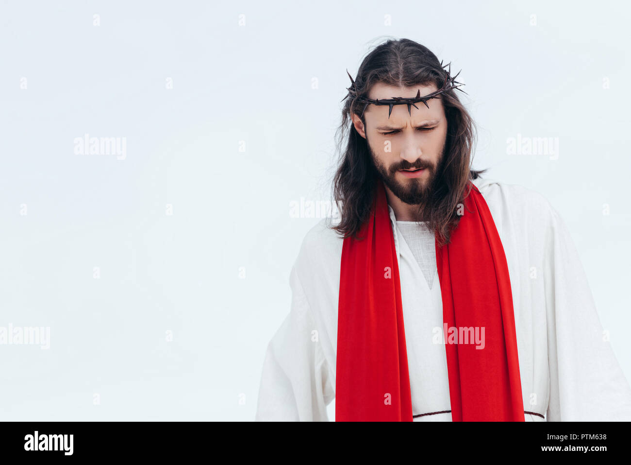 Jesus in robe, red sash and crown of thorns looking down against light