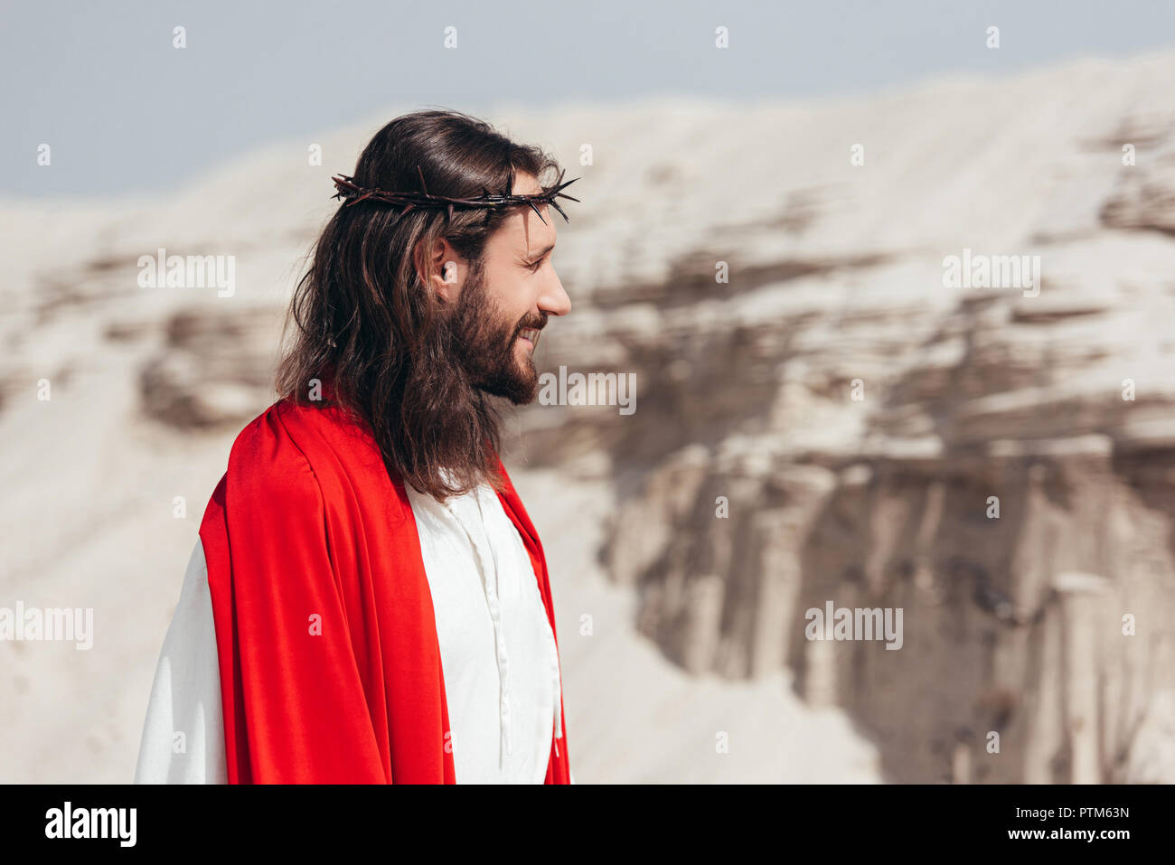 side view of smiling Jesus in robe, red sash and crown of thorns ...