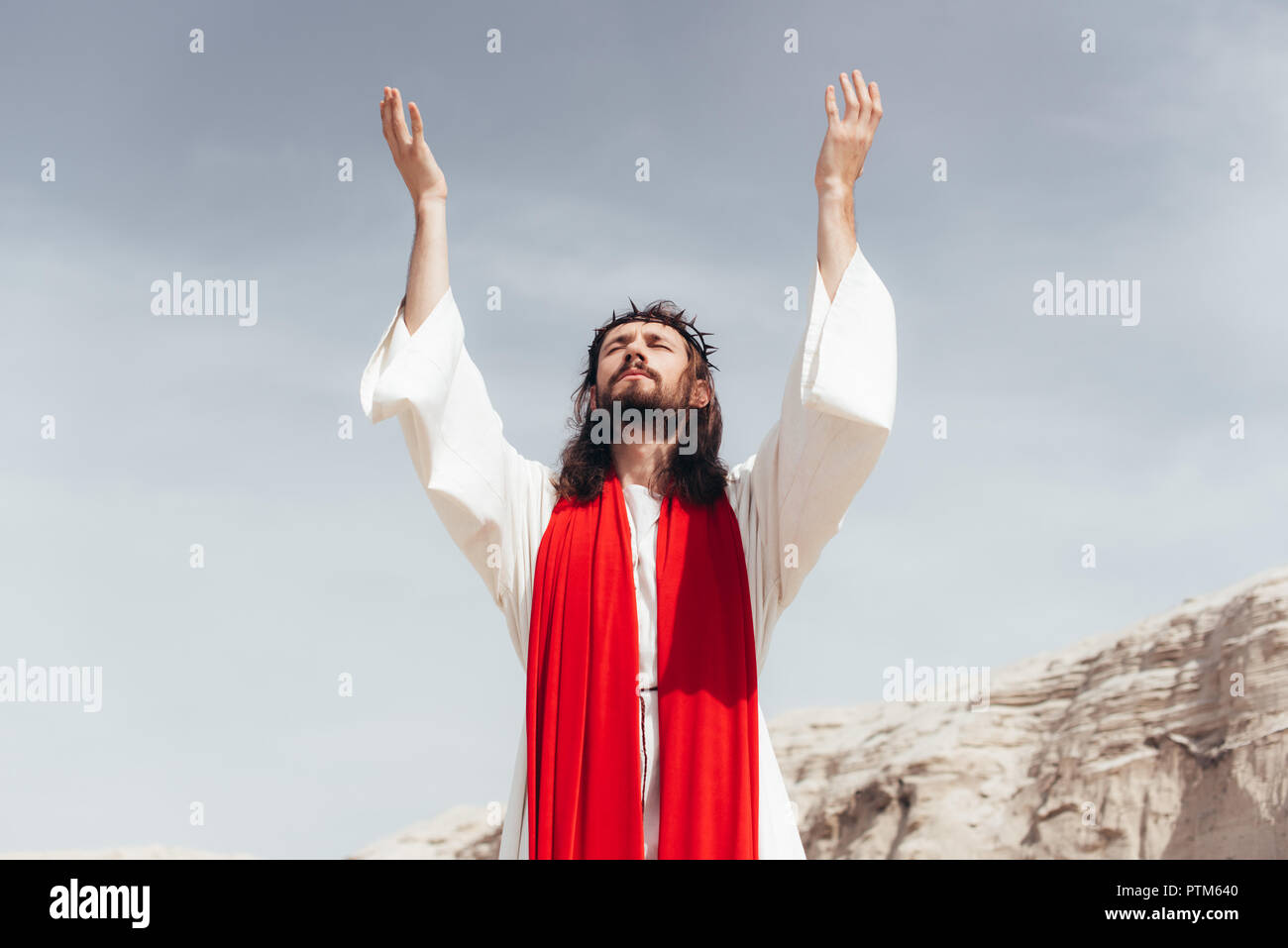 Jesus in robe, red sash and crown of thorns standing with raised hands ...