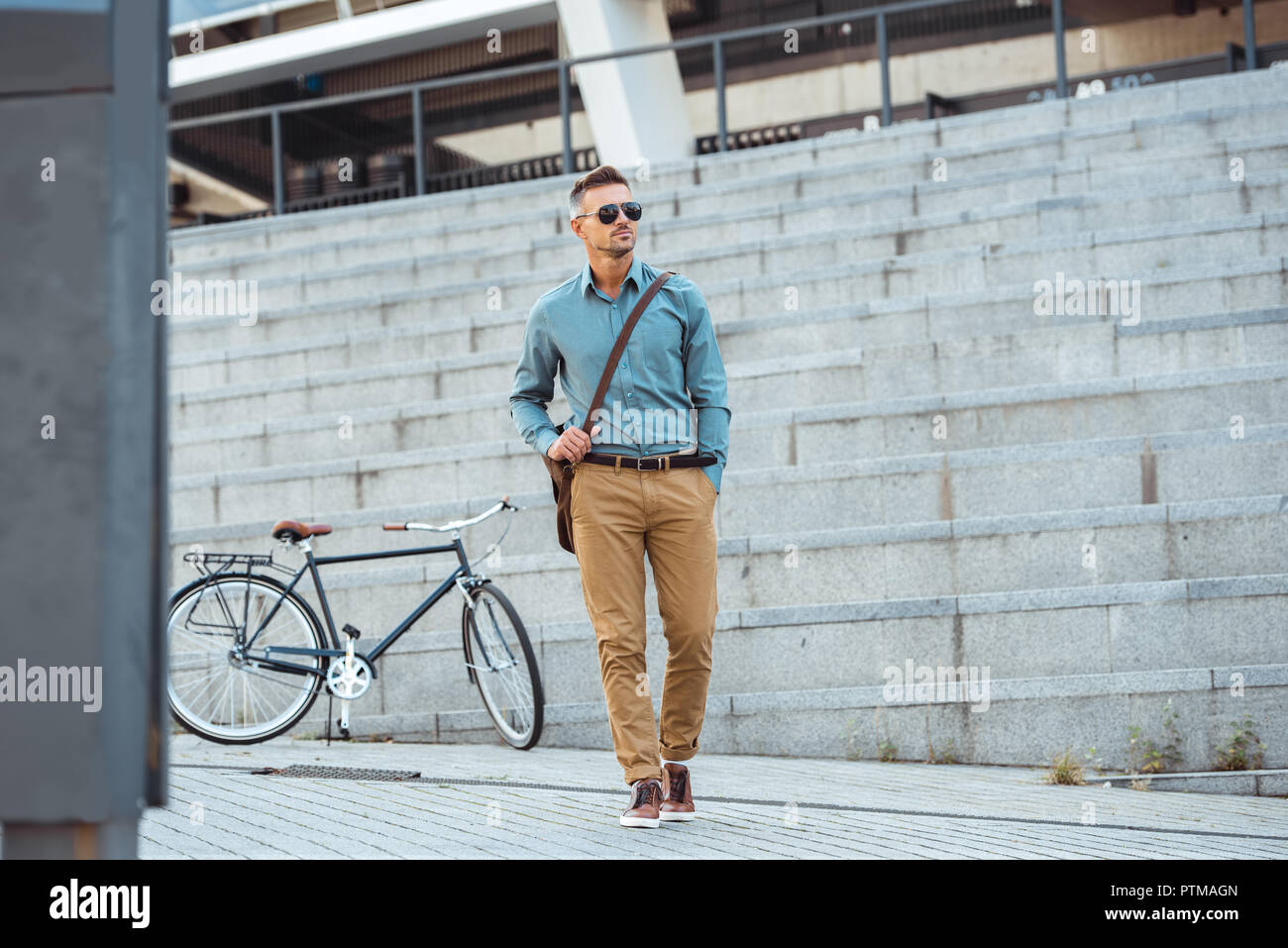 handsome middle aged businessman in sunglasses walking on street, bicycle on background Stock Photo