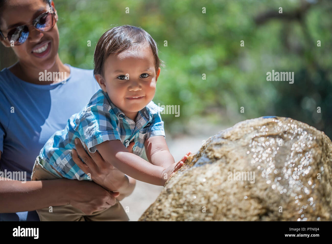 Latino mother holding her 2 year old boy as he plays with a water fountain during summer vacation Stock Photo