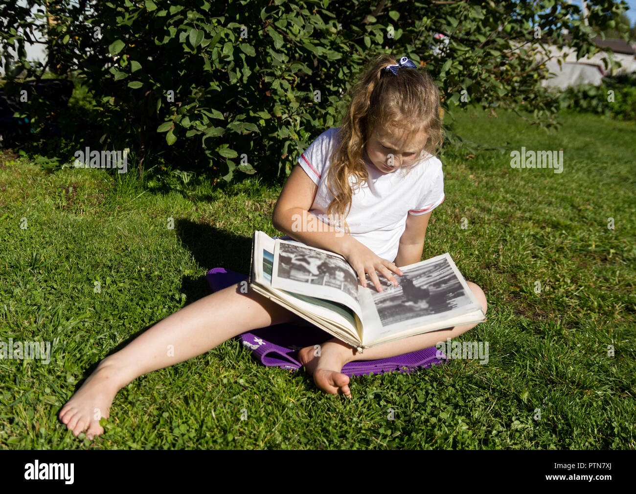 Beautiful teenage girl sitting on a grass in summer park and reads book Stock Photo
