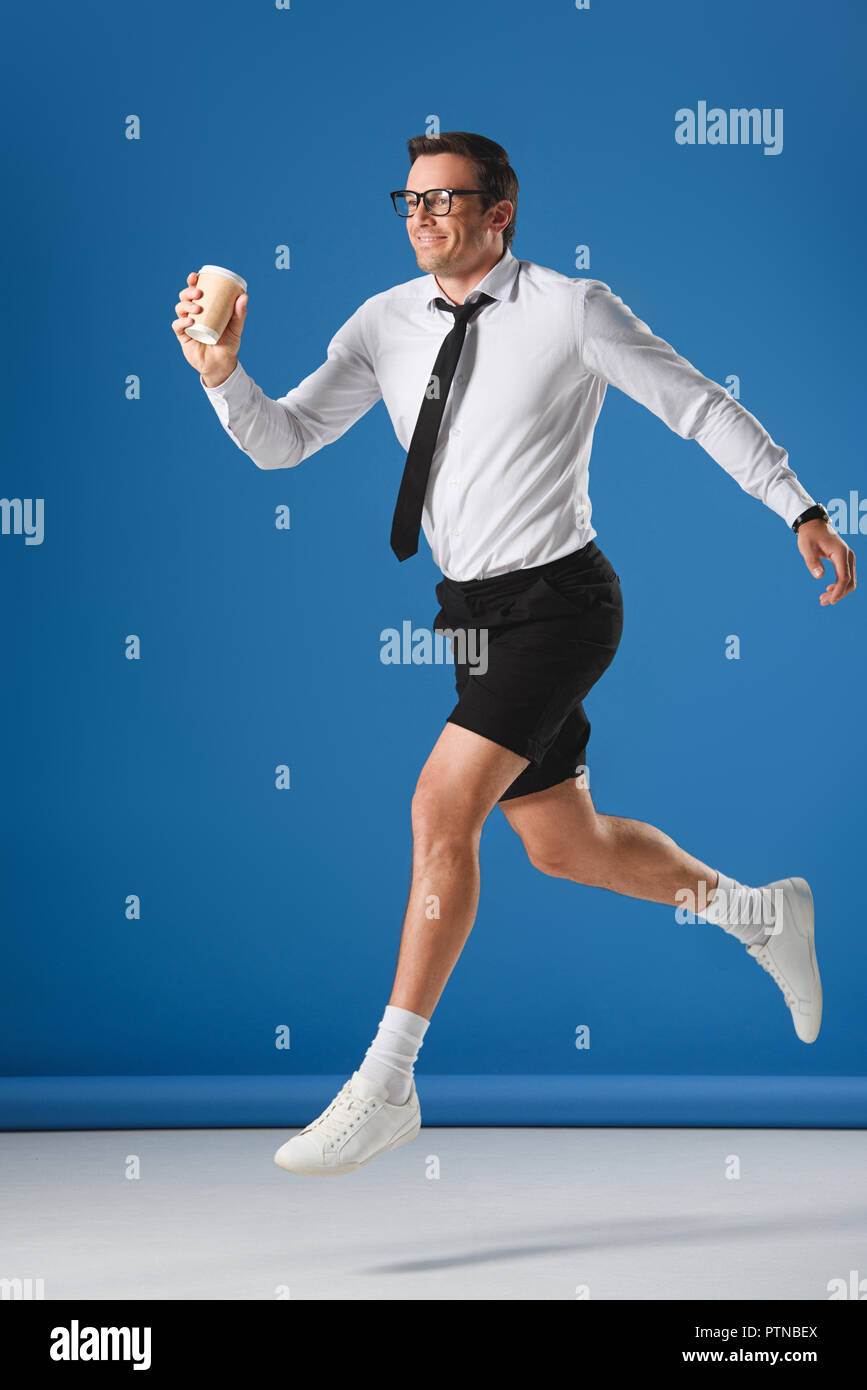 happy man holding disposable coffee cup while jumping and looking away on blue Stock Photo