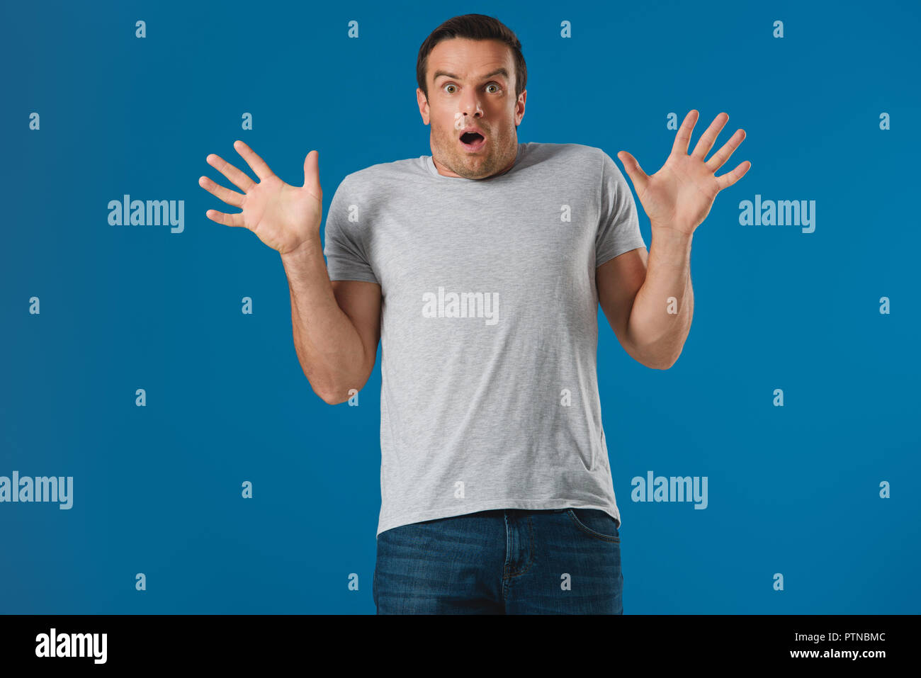 shocked man raising hands and looking at camera isolated on blue Stock Photo