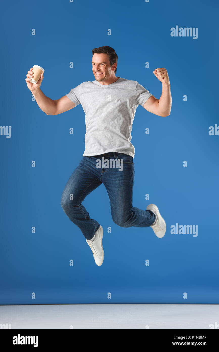 excited man with coffee to go jumping and triumphing on blue Stock Photo