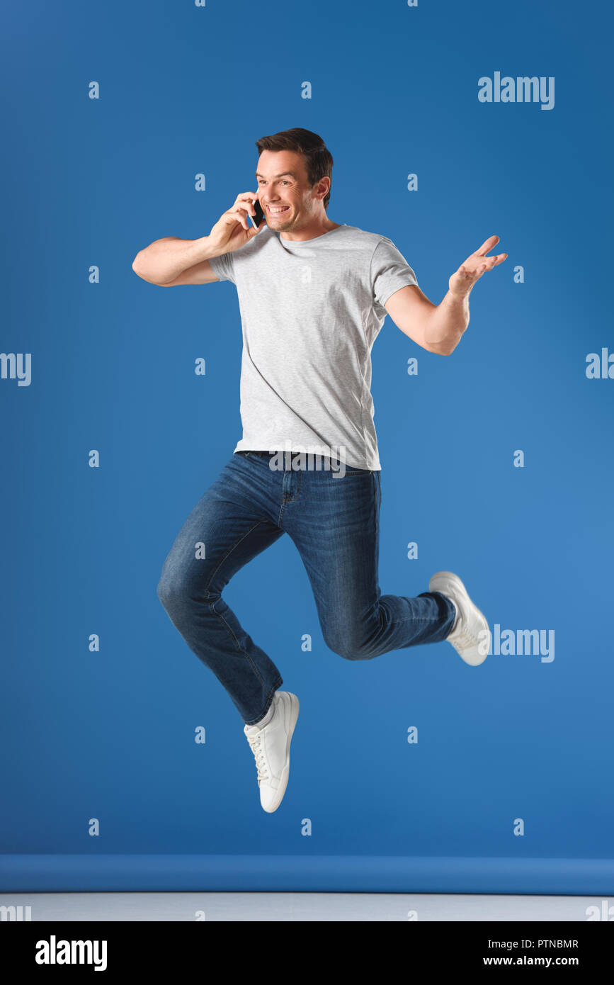 happy man talking by smartphone and jumping on blue Stock Photo
