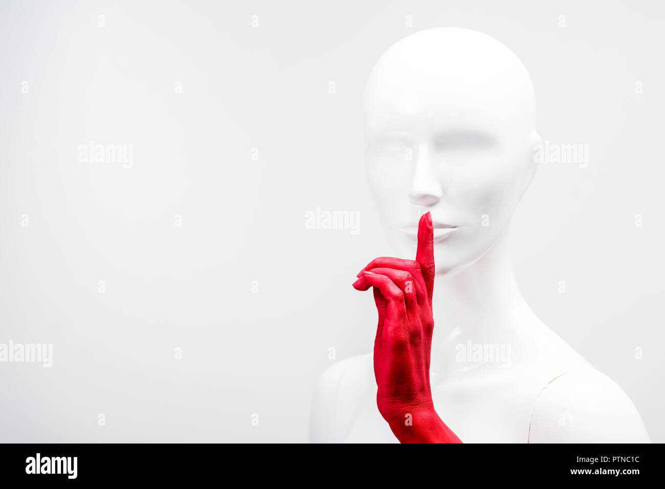 cropped image of woman in red paint showing silence gesture with mannequin isolated on white Stock Photo